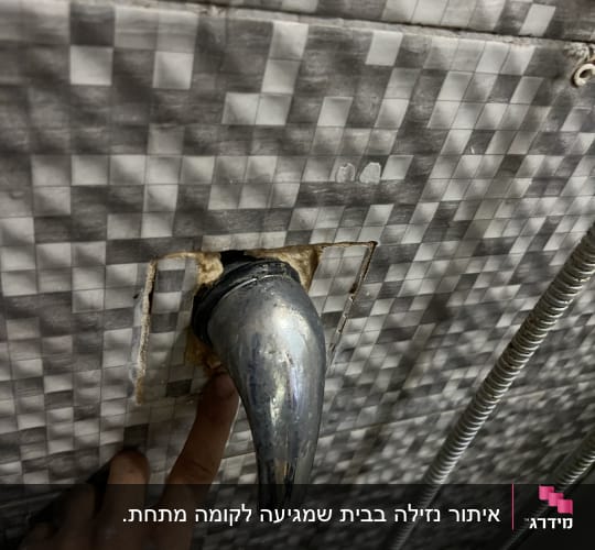 ברז מתכת בקיר אריחים עם אצבע מצביע על חיבור